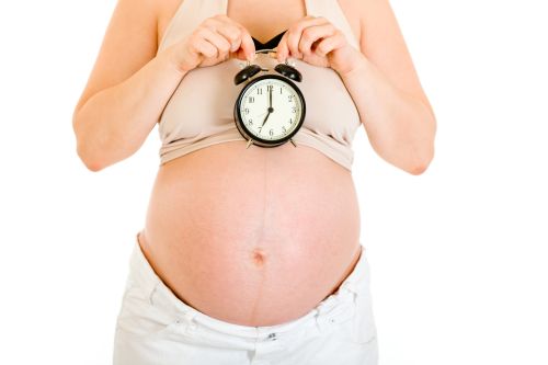 Pregnant woman holding alarm clock near her tummy isolated on white.  Close-up.