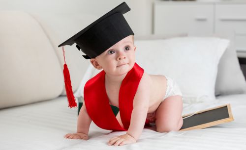 Adorable 10 months old baby boy in graduation cap crawling on bed