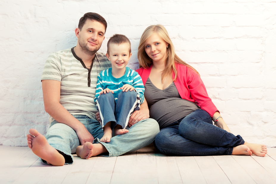 Happy family of three sitting on the floor near the wall:  mother, father and little boy. Mother is pregnant.
