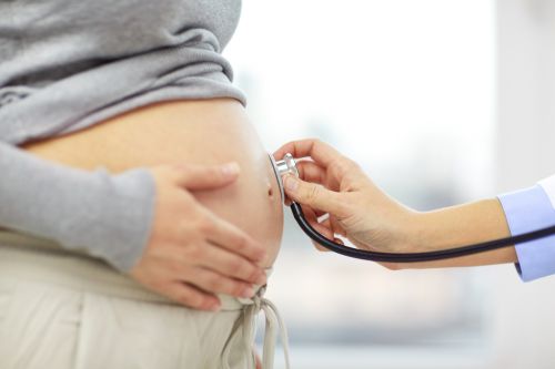 pregnancy, healthcare, people and medicine concept – close up of pregnant woman belly and doctor hand with stethoscope at medical appointment in hospital