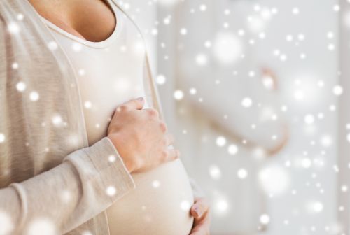 pregnancy, motherhood, winter, people and expectation concept – close up of pregnant woman belly and hands over snow